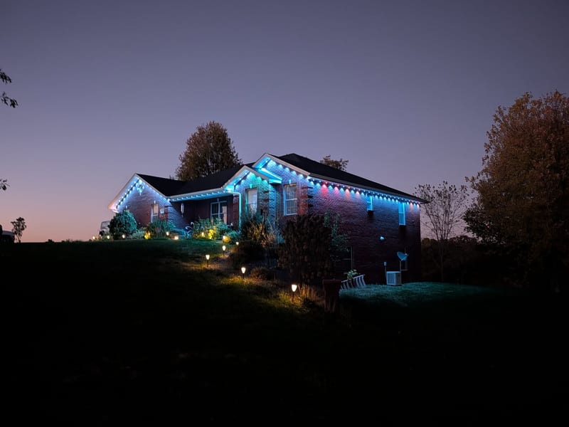 Brick ranch home with permanent teal and blue roofline LED lighting at dusk