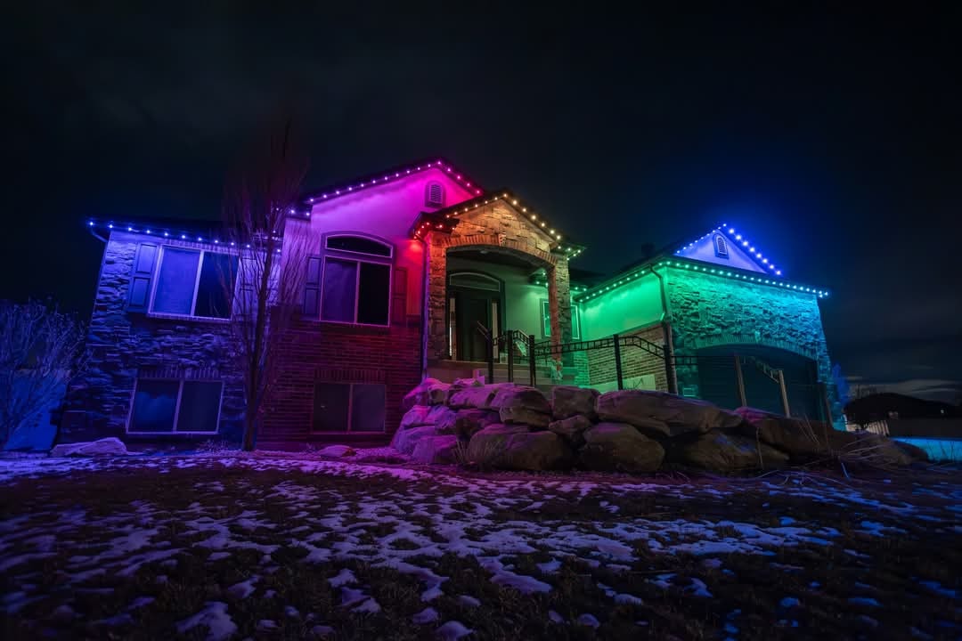 Two-story brick home with permanent rainbow roofline LED lighting at night
