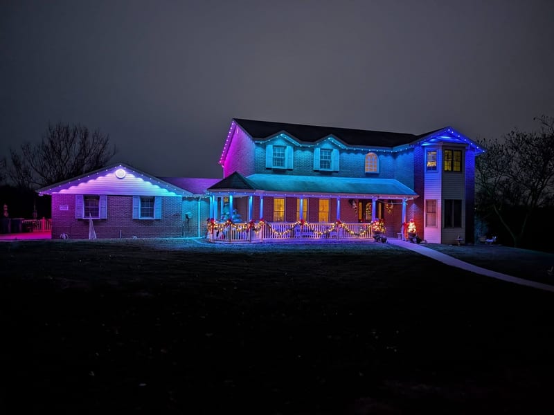 Two-story home with permanent pink teal and blue roofline LED lighting at night