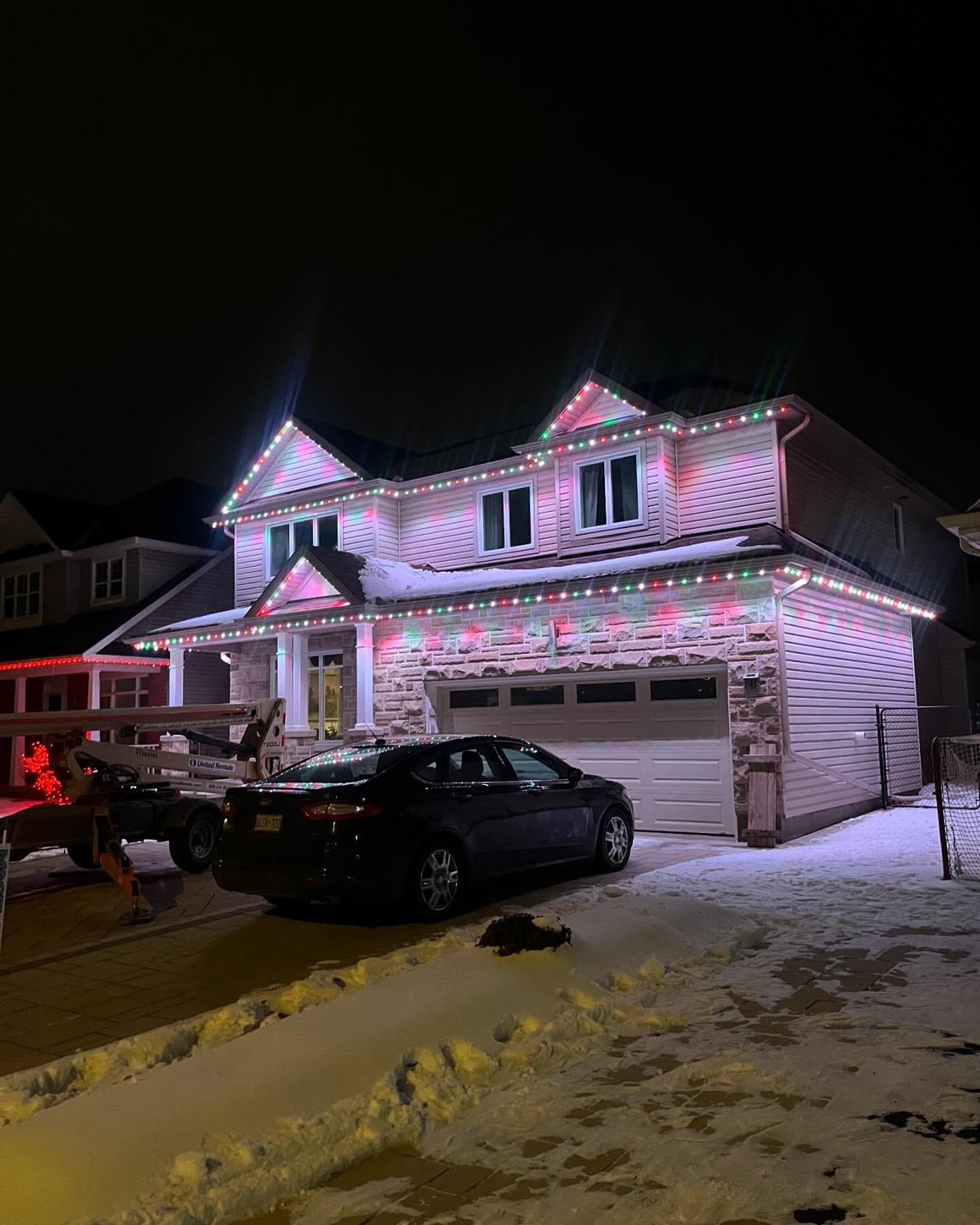Two-story home with permanent red and green roofline LED lighting in winter snow